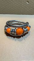 Coiled bangle showing orange beads and metal spacers