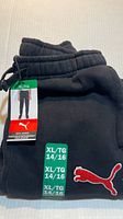 Folded black Puma joggers showing waistband, hangtag, size sticker and red logo