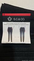 Front packaging label on folded black pants showing brand, style, size 8