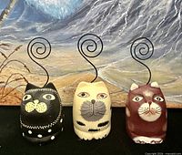 Front view of three painted wooden cat figurines with spiral wire tails