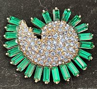 Front view of gold-tone brooch showing green baguette crystals and blue pavé center