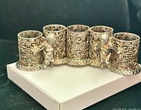 Front view of gold-tone filigree lipstick holder with four cylindrical slots and cherub figures