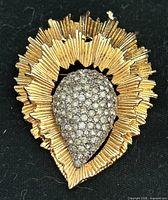 Front view showing gold-tone starburst rays and pavé rhinestone teardrop center