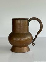 front view of hammered copper pitcher with flared base and twisted handle