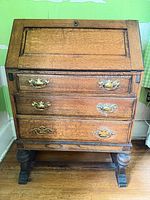 Front view of closed oak drop-front desk showing three drawers and brass hardware