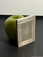 Entire sterling silver calling card case standing beside apple for scale, showing engine-turned pattern, borders, and overall size