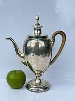 Full frontal view of sterling silver chocolate pot beside apple for scale