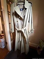 Full view of trench coat hanging, shows exterior color, length, belt and epaulettes