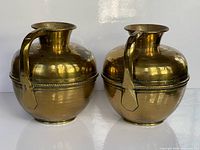 Front view of both brass pitchers showing shape, mid-band and patina
