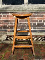 Full view of oak bar stool showing round seat, legs, stretcher rungs, finish wear