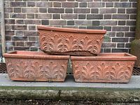 Stack of three rectangular terracotta planters showing oak leaf design and overall wear