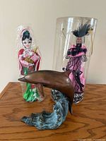 Group shot of Chinese opera doll, Victorian doll in case, and bronze dolphin figurine on table