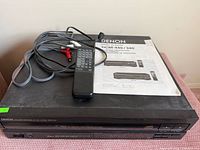 Top view of Denon DCM-440 CD changer with remote, RCA cable and manual on unit