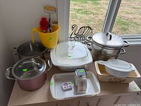Group shot of all cookware, bakeware, pitcher, trivet, scale and timer on cabinet