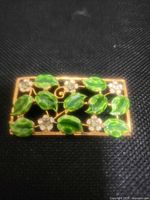 Front view showing green enamel leaves, rhinestone flowers, gold-tone frame