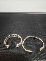 Two silver-plated open cuff bracelets side by side: braided and twisted designs