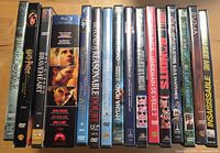 Row of 17 movie discs, mix of DVD and one Blu-ray, titles visible on spines