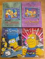 Front view of four sealed The Simpsons DVD box sets for seasons 2,3,7,12