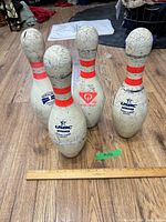 Front view of four bowling pins standing on wood floor with ruler for scale
