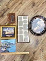 Overview of five items arranged on floor: collage frame, oval art print, two framed prints, decorative plaque and ruler for scale.