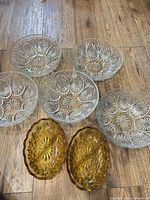 Group shot of five clear glass bowls and two amber trays on wood floor
