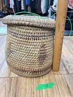 Lidded woven basket next to ruler showing height