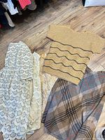 Overview of knit top, plaid skirt, two cream lace garments on floor