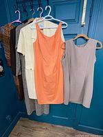 Five dresses displayed on hangers: brown, patterned grey, yellow, orange, taupe