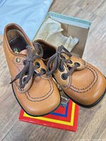 Pair of tan leather lace-up children’s dress shoes resting on colorful shoe box
