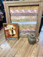 Group shot of framed fabric collage, framed Gervais ad print, and metal teapot