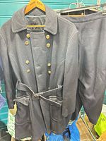 Front view of wool coat on hanger next to one pair of pants