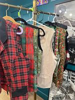 Five vests hanging: red plaid, tartan, green patterned, beige, floral