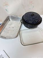 All three kitchenware items grouped: aluminum roasting pan, glass baking dish, enamelware Dutch oven with lid
