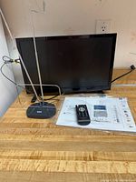 Front view of Insignia TV with antenna, remote and paperwork on counter