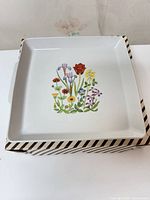 square Naaman porcelain platter with floral design on top of striped box