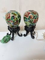 Full view of both floral glass lamps on black wood stands with cords visible