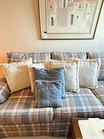 Five pillows displayed on plaid sofa: three cream with fringe, one medium blue dotted, one small blue jacquard