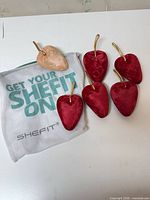 Five red and one peach velvet heart shoe inserts with gold loops and SHEFIT mesh bag
