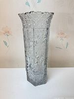 Full view of tall hexagonal clear cut glass vase showing floral engraving and scalloped rim