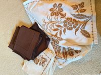 Folded embroidered tablecloth, 8 matching embroidered napkins, and stack of 10 solid brown napkins