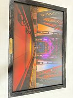 Front view of framed print showing multicolor image, distressed black frame, glass, gold plaque