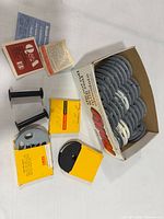 Open Kodak carton containing stack of grey/white plastic reels, loose black spools, Kodak boxes, paper inserts visible