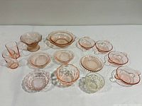 Full lot showing all fourteen pieces of pink and clear depression and cut glassware on white surface