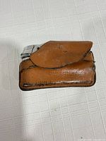 Silver pocket lighter partially inserted in brown leather snap-flap pouch on white surface