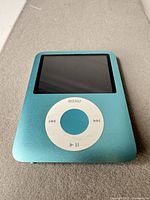Front view showing turquoise anodized face, screen, click-wheel