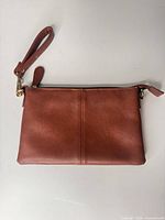 Front view of brown leather wristlet clutch with wrist strap attached.