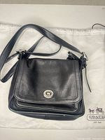Full view of Coach black leather crossbody on white Coach dust bag