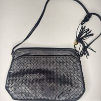 Full view of black woven-front leather crossbody bag with strap