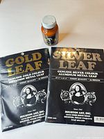 Front view of gold and silver leaf packs with adhesive bottle