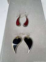 Two pairs of enamel dangle earrings on display pad